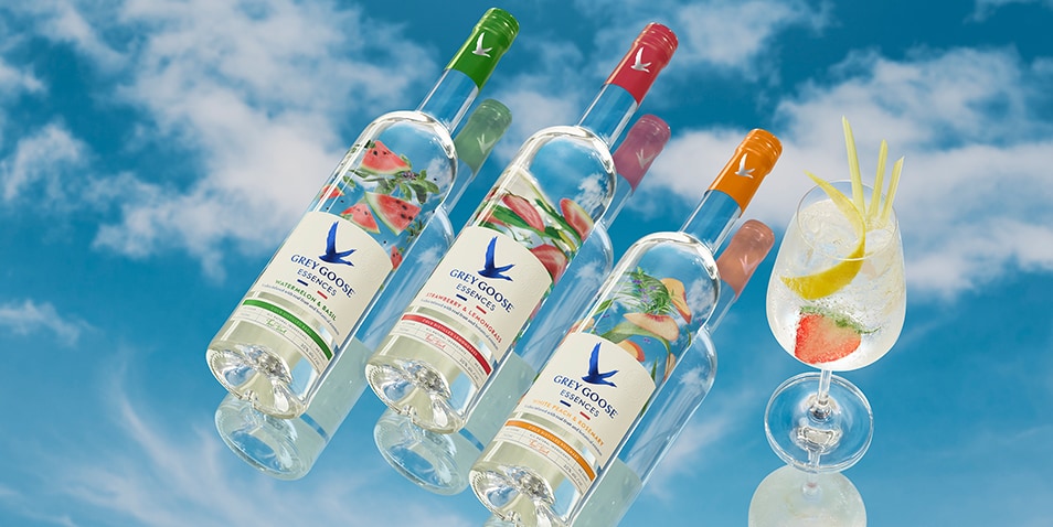 Three bottles of Grey Goose Essences and a Strawberry and Lemongrass Vodka Spritz cocktail.