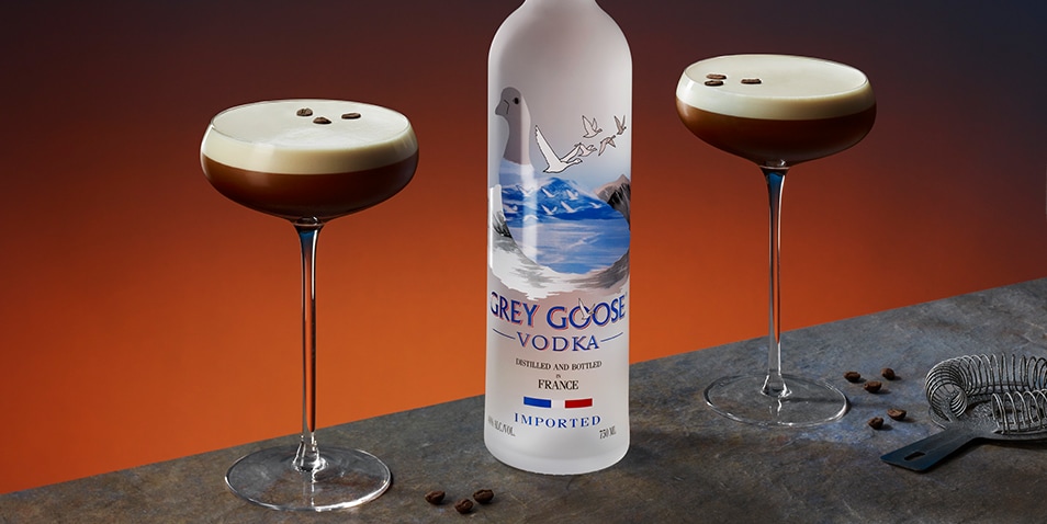 A bottle of Grey Goose vodka and two Espresso Martini Cocktails garnished with three espresso beans.